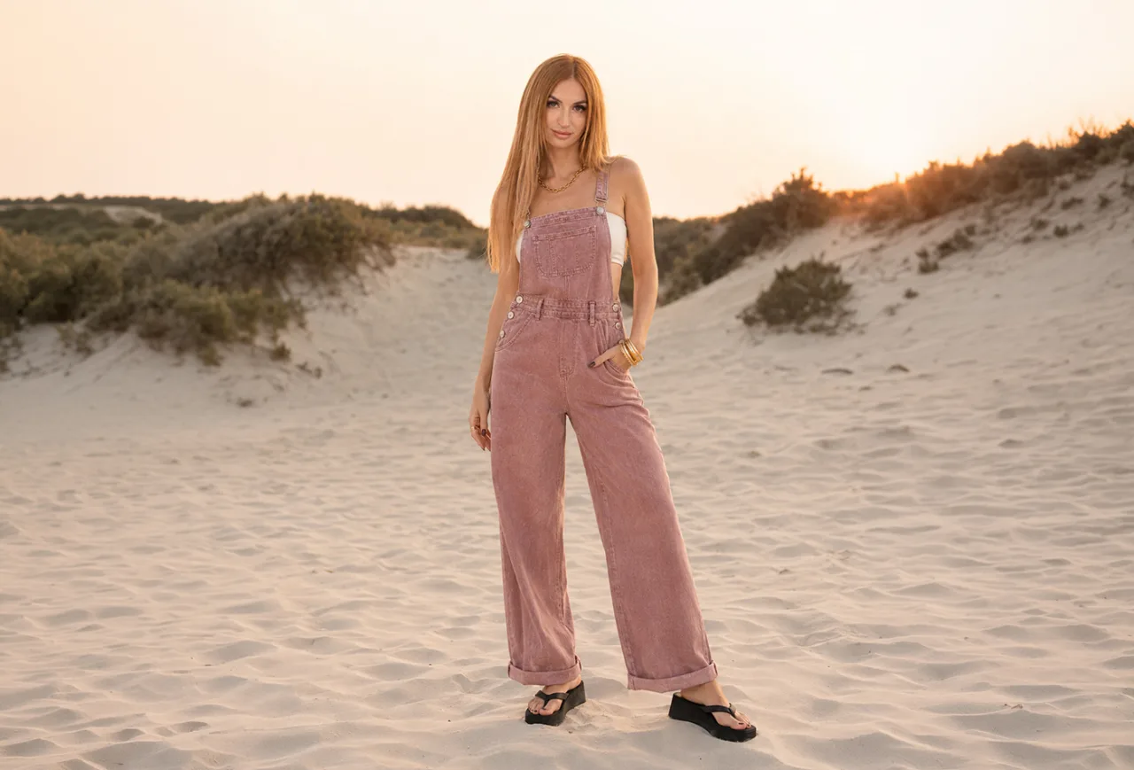 Bamby Doll standing in pink overalls on sand dunes at sunset